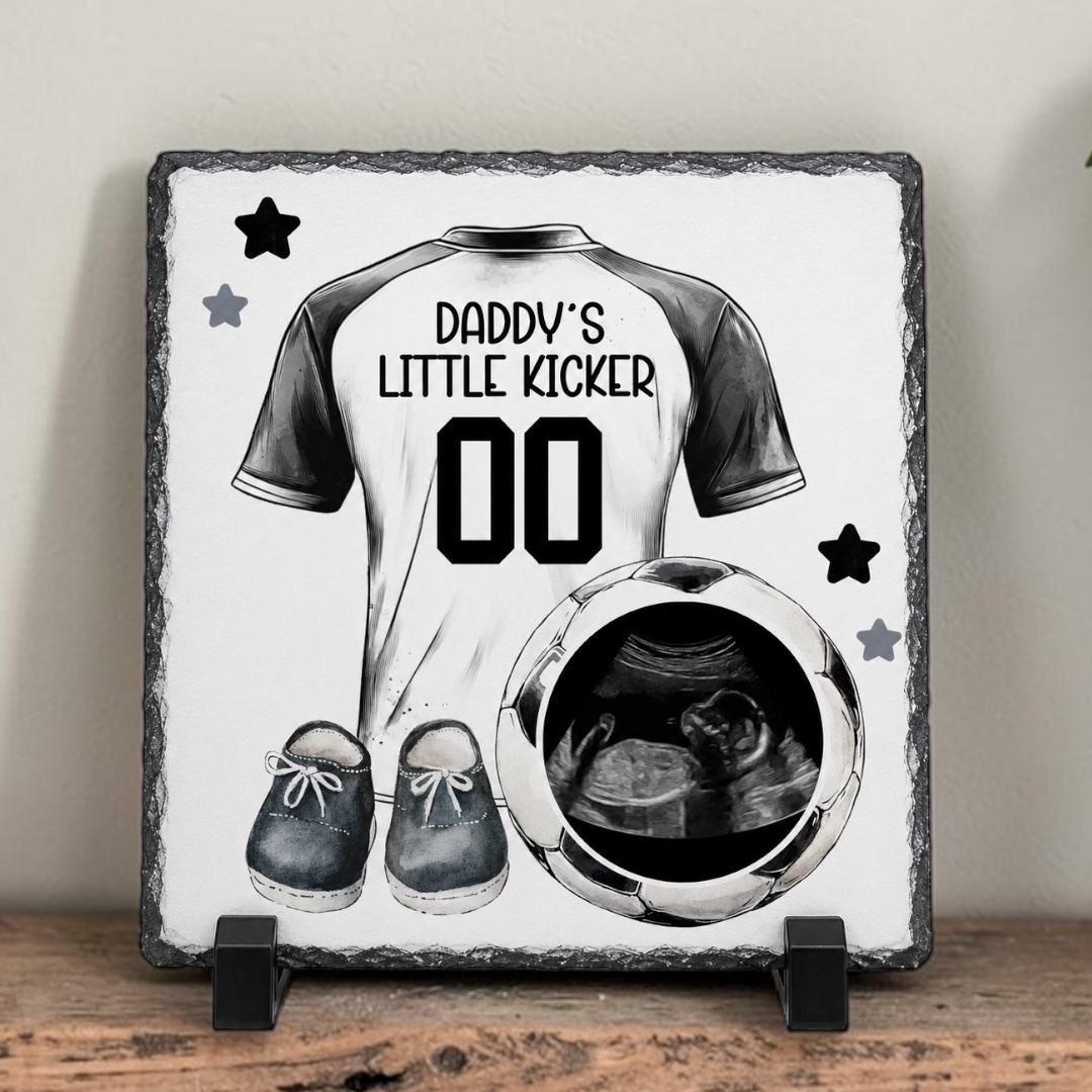 Decorative slate with a t-shirt design, shoes, and ultrasound photo on a wooden surface.