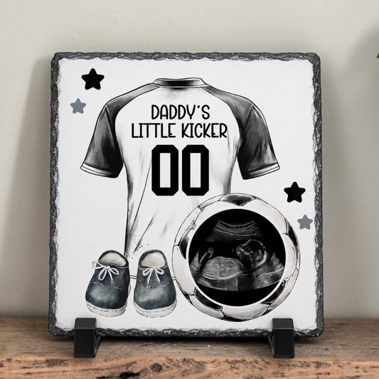 Decorative slate with a t-shirt design, shoes, and ultrasound photo on a wooden surface.