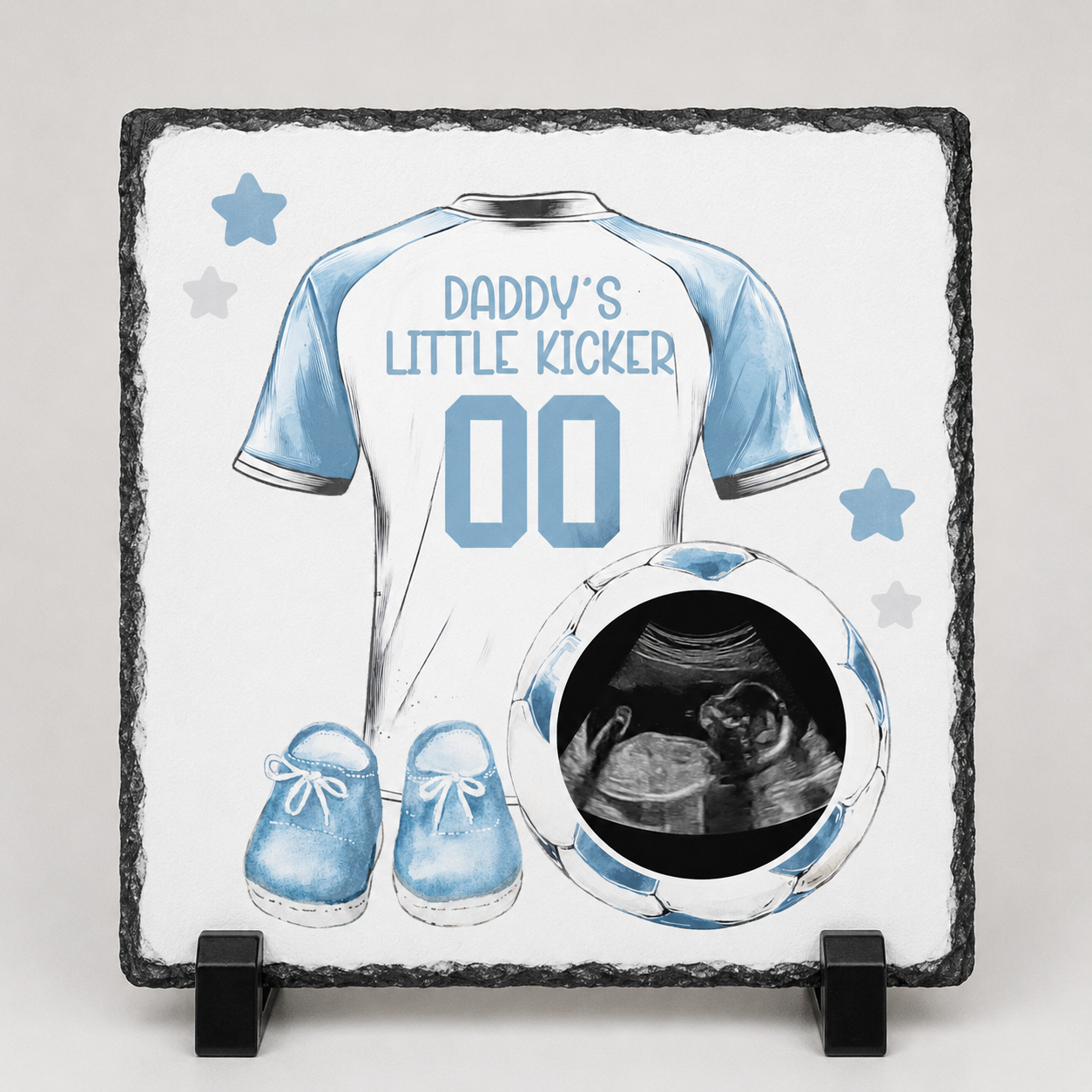 Decorative slate with a baby shirt design, shoes, and ultrasound photo on a white background